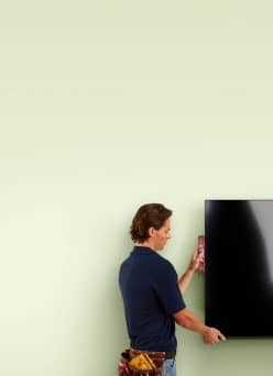 An image of a person mounting a TV on a green wall.